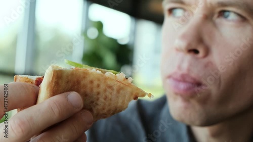 A man in a restaurant holds a slice of pizza and carefully chews a bitten piece. Perfect 4K video for food ads, restaurant promos, and culinary content.