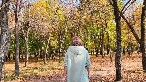Slow motion picture of a sad woman walking along a path in an autumn park.
