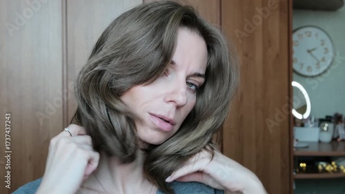 A feminine young woman runs her hand through her hair and looks at the camera.