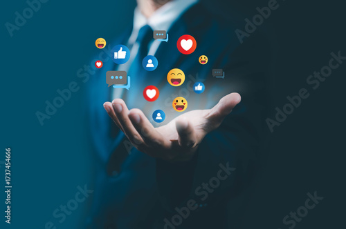 Businessman hand holding floating social media icons with like, heart, emoji, and comment, symbolizing digital marketing, online engagement, social communication, and brand connection.