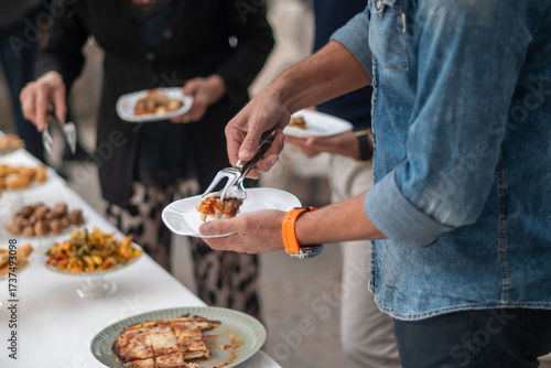 Guests at an elegant private event enjoy a gourmet buffet selection of delicious catered food items displayed on a long table in a bright airy venue with people serving themselves from various dishes