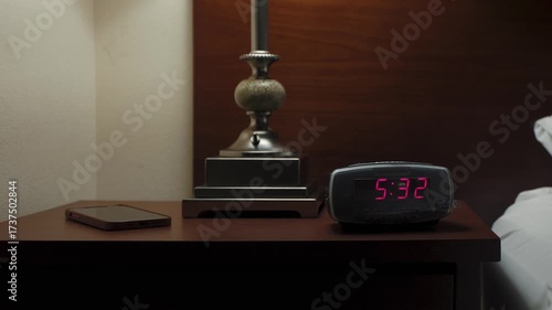 In a dark room, an alarm clock glows on a nightstand. A person turns on the light and shuts off the alarm, ideal for morning, sleep, and lifestyle visuals.