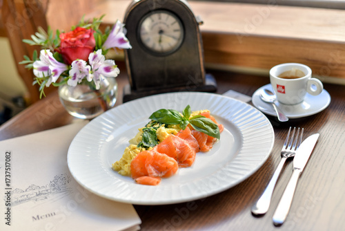 breakfast salmon with omelet on a white plate on a brown table with coffee and a retro clock