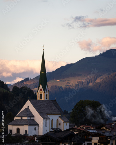 Canvas Print Kirchberg in Tirol parish church with green steeple at sunrise, surrounded by alpine mountains and village houses
