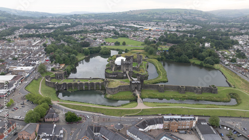 Aerial view of the formidable Caerphilly Castle rises from its reflective moat, ancient stone against modern town, a timeless fortress, Caerphilly, Wales, United Kingdom.