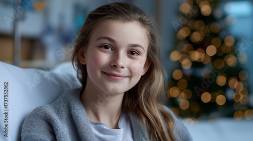 Young girl smiling, enjoying the holidays with a joyful expression while relaxing at home, celebrating christmas with a festive decorated tree in the background