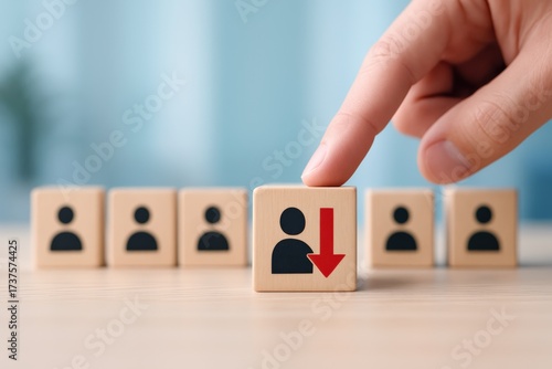 Business hand points to a wooden cube featuring a downward red arrow, clearly symbolizing employee layoffs, corporate downsizing, and workforce reduction decisions