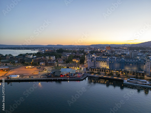 Aerial view of a city's waterfront glows with warm lights reflecting on the tranquil water under a dusky sky, Oslo, Oslo, Norway.