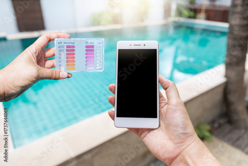 Smartphone and water tester in girl hand over swimming pool background, online quality control on smartphone