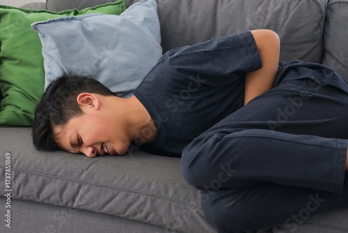 Young Boy Clutching Stomach Suffering from Severe Abdominal Pain on a Couch in Living Room