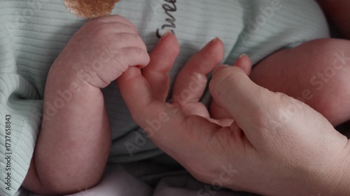 Newborn baby hand holding adult finger indoors, closeup detail, symbolizing connection, tenderness, care, motherhood and family love.