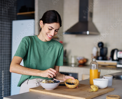 Portrait of a young woman preparing and eating breakfast, drinking juice in the kitchen at home