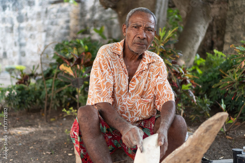 Elderly craftsman carving wood outdoors with traditional skill