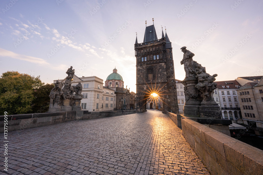 Fototapeta premium Stunning sunrise over Prague with warm golden light illuminating historic architecture, cobblestone streets, and iconic city landmarks in high-quality detail.