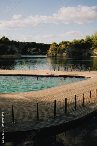 Wooden pier over beautiful artificial lake with crystal clear water and tourists swimming, surrounded by rocky cliffs and green vegetation, perfect place for summer vacation. Wooden pier, rocky cliffs