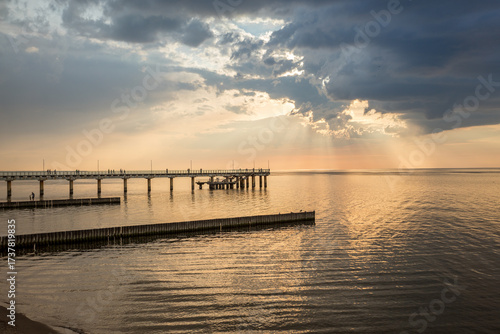 The Baltic Sea at sunset. A beautiful seascape with orange and gray clouds and a pier in the foreground. The city of Zelenogradsk and the embankment