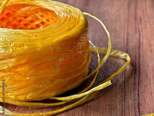 Close-up of yellow raffia plastic rope roll on wooden surface. Strong, durable, and flexible cord used for packaging, shipping, agriculture, DIY, and craft projects.