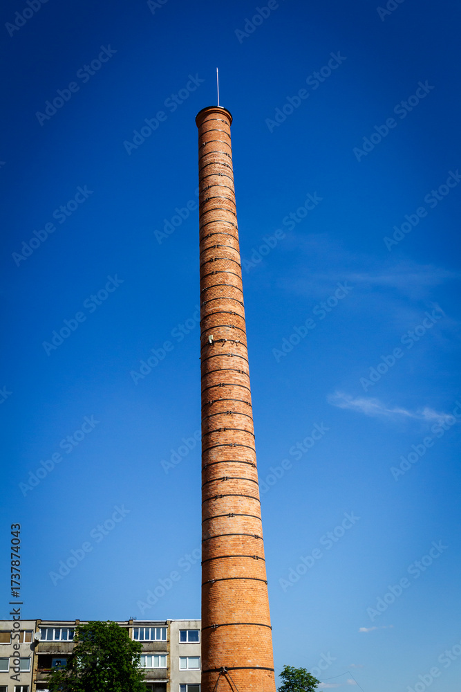 Fototapeta premium Old tall factory chimney made of bricks against blue sky.