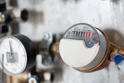 Close-up of analog water meter with pressure gauge mounted on pipe system. Concept of household utilities, consumption monitoring, energy efficiency and infrastructure management.