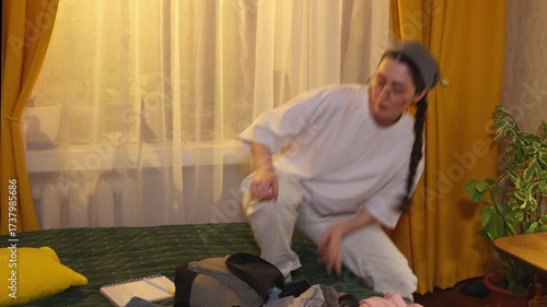 Female student arranges clothing and accessories on bed folding and packing items for upcoming holiday journey. Mid shot