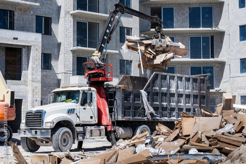 Cleanup and debris removal, heavy equipment with jawbone bucket used to pickup debris and deposit in commercial dump truck for hauling away, in residential building construction site