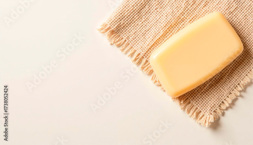 A smooth yellow bar of soap rests on a natural textured cloth, highlighting a sense of cleanliness. The soft colors create a calming and inviting atmosphere