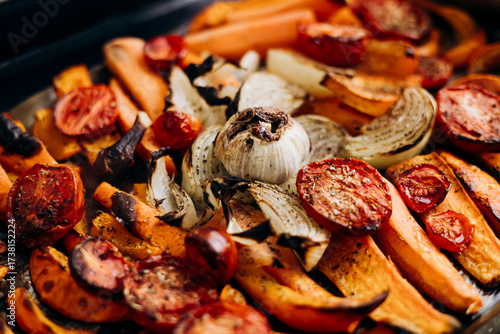 Roasted autumn vegetables pumpkin tomato onion garlic on baking tray, close up.