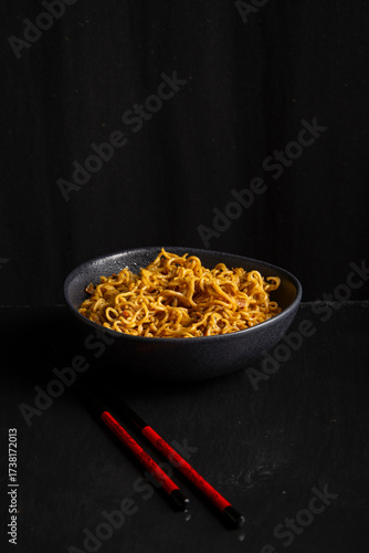 View of a bowl of noodles with chopsticks, black background, vertical with copy space