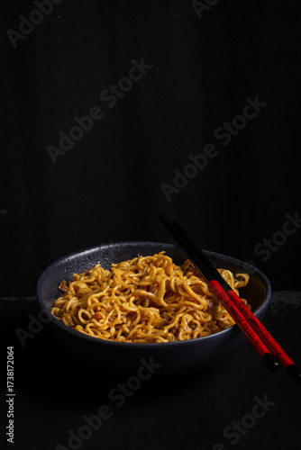 Top view of a bowl of noodles, chopsticks, black background, vertical with copy space