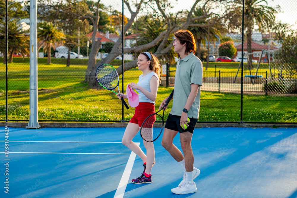 © Austockphoto - Two young adults walk together on a blue tennis court, ready for a friendly game © Austockphoto - Two young adults walk together on a blue tennis court, ready for a friendly game