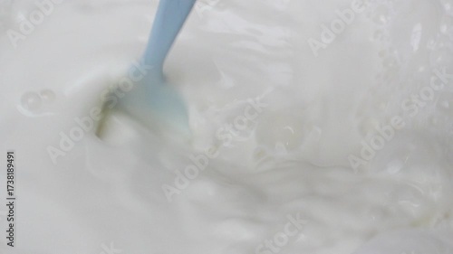 Close-up spoon stirring foamy milk with visible bubbles and smooth texture freshness and lightness of dairy, Concepts related to food preparation health and natural ingredients.