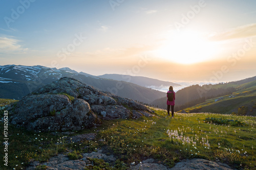 Obraz na plátně Female traveler observes a vibrant dawn from a flowery alpine meadow, peaks visible above mist