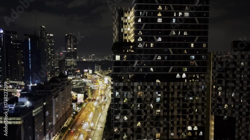 A nighttime view of Kuala Lumpur featuring a modern residential tower with illuminated windows, surrounding skyscrapers, and brightly lit highways that highlight the vibrant cityscape of Malaysia
