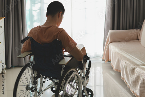 View from the back of a young man with disability in wheelchair with door background and nature light. Feeling sad, lonely and isolated, waiting for something, Concept caring for patients.