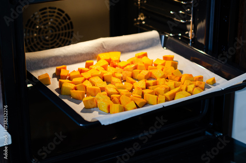 Close up of bright orange cut pumpkin cubes in baking tray inside oven ready for roasting