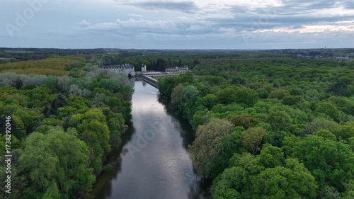 Aerial view of Château de Chenonceau over the river, the lush green trees contrast against the gray water, Chenonceaux, Centre-Val de Loire, France.