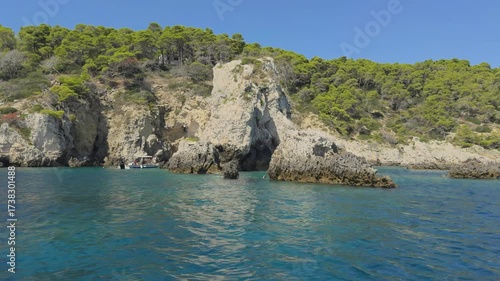 Rocky coastline with turquoise sea and boats cruising under a clear blue sky.