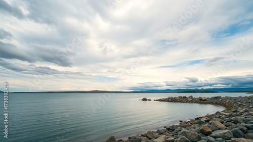 Serene waters meet a rocky shore under a dramatic, cloudy sky, evoking a sense of tranquility and the vastness of nature's beauty along the coast line location.