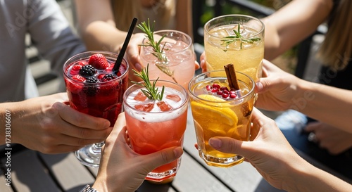 Group of friends toasting with colorful summer cocktails outdoors.
