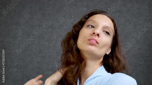 A beautiful girl with curly long hair in a blue blouse, 18-25 years old, adjusts her hair with her hands and is pleased with herself