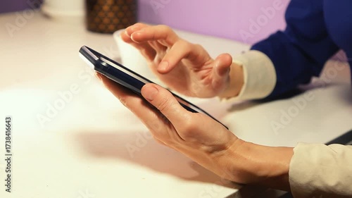 Close up of a businesswoman using a mobile phone and drinking coffee from cup sitting on the table