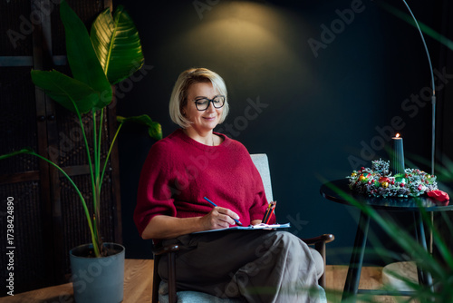 Woman drawing work-life balance wheel sitting on armchair at cozy dark home interior. Self-reflection and life planning for next new year. Personal Year review. Coaching tools. Finding Balance in Life