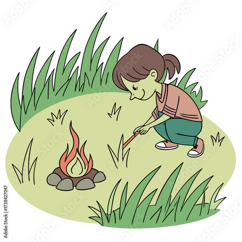 A young child crouches down in the grass carefully tending to a small campfire with a stick