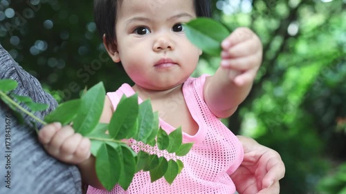 Baby holding a branch with leaves, exploring nature with curiosity and early childhood learning