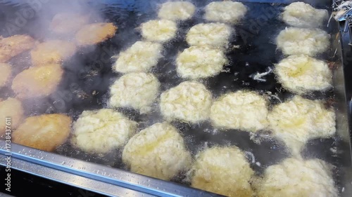 Man is frying Reibekuchen patato pancakes food in a pan at Christmas market in Germany. The street food is golden brown and looks delicious