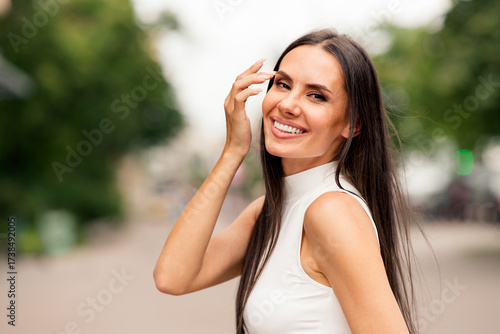 Beautiful young woman outdoors smiling confidently, showcasing elegance and charm in urban setting with natural lighting