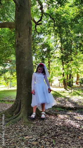 A girl in a white dress and a veil, the image of a scary bride, moves like a zombie on the street, in the park on Halloween