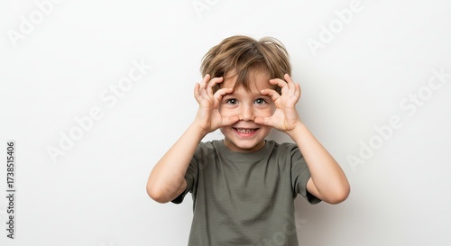 Excited young boy making funny faces holding hands around eyes isolated on white background