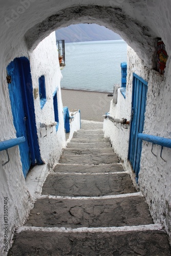 Narrow, stone steps descend through a white-washed archway towards a tranquil sea view