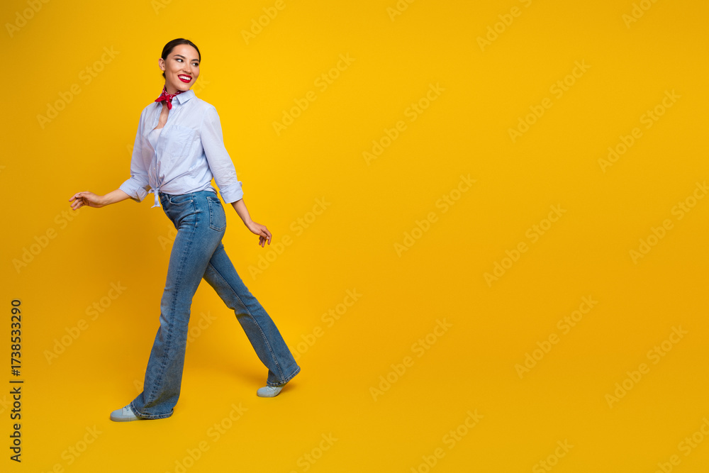 Fototapeta premium Attractive young woman walking confidently against yellow background showcasing modern style and cheerful personality